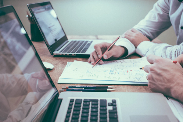 Two people sat at a desk with laptops and paperwork